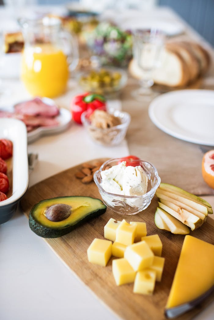 A vibrant breakfast spread featuring cheese, avocado, fruit, and more on a wooden board, perfect for food lovers.